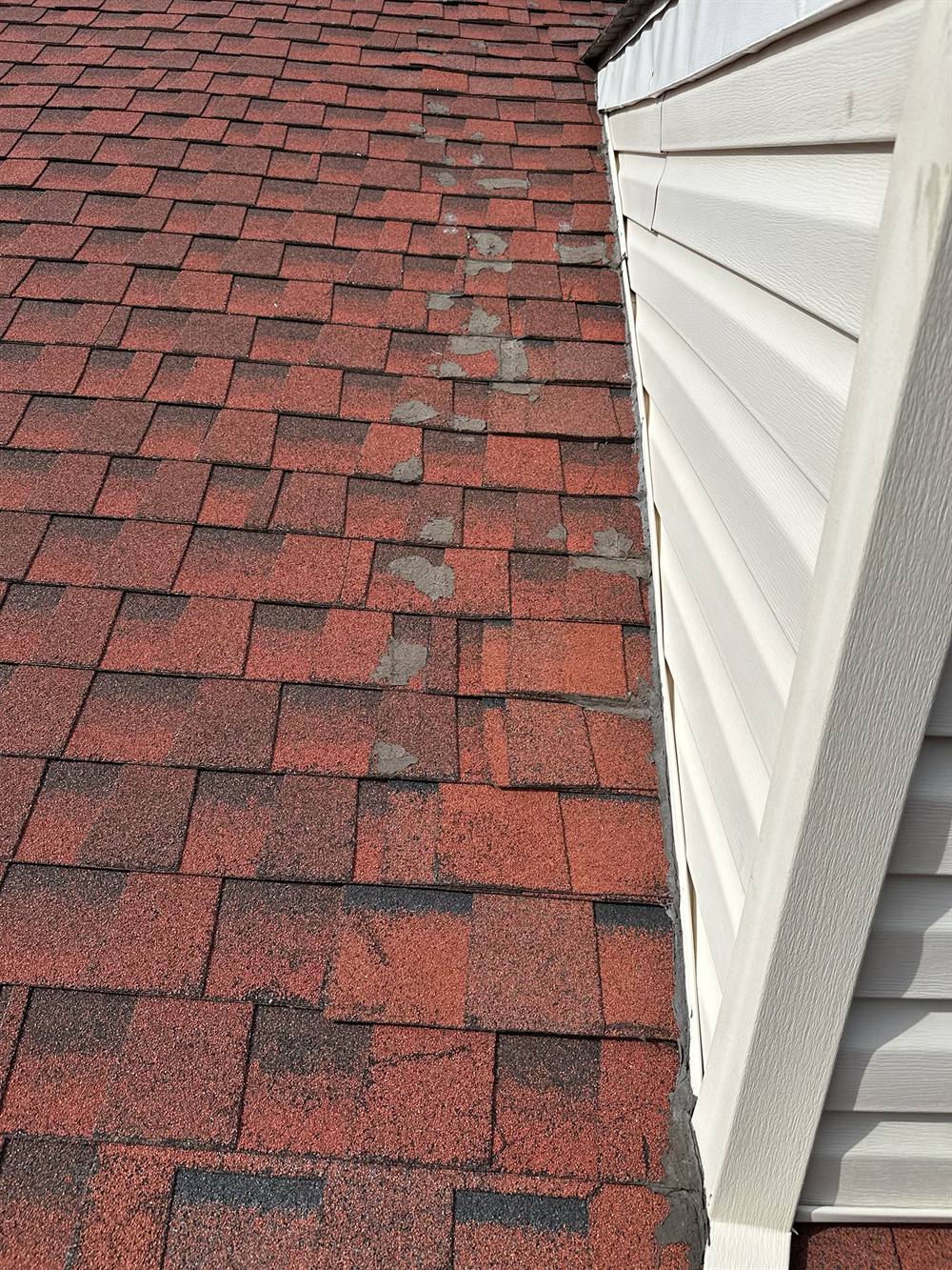 Failed tar patches smeared over shingles on a roof