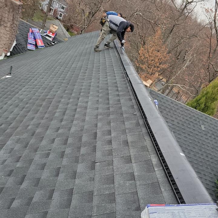 Roofer fastening a new ridge vent along the peak of a freshly shingled roof