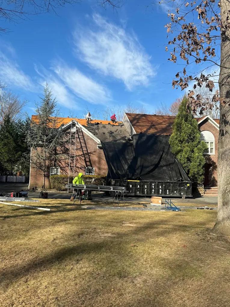 Sigma crew tearing off an old roof on a brick home, with tarps and a dumpster protecting the yard